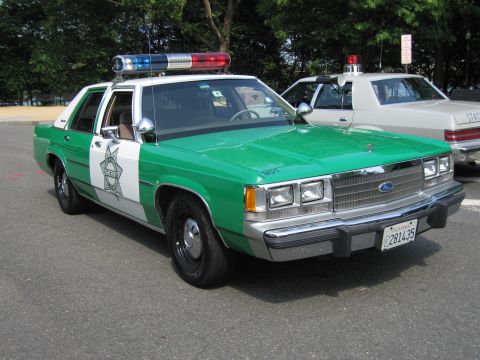 1991 Ford Crown Victoria - A green and white police car is parked on asphalt, with a second white police car visible behind it.