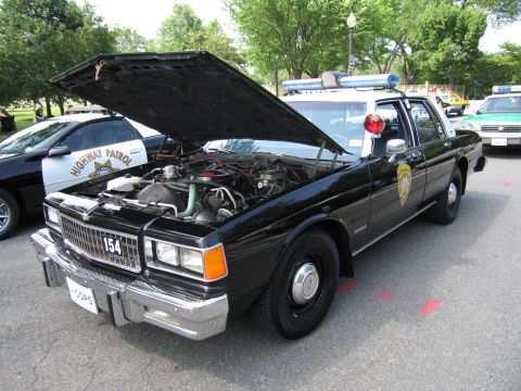 1991 Ford Crown Victoria - A black police car with its hood open is parked next to a highway patrol vehicle.