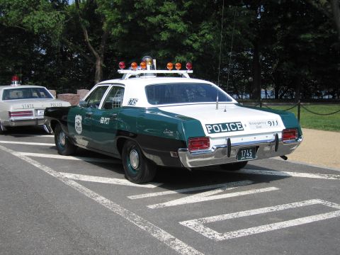 1991 Ford Crown Victoria - This police car, likely from the 1970s, is parked next to another vehicle on a paved surface.