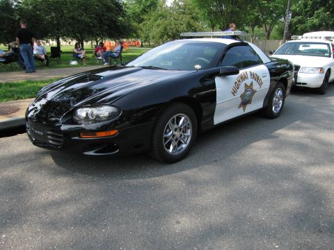 1991 Ford Crown Victoria - A black Chevrolet Camaro is marked as a highway patrol vehicle, parked on a street with people in the background.