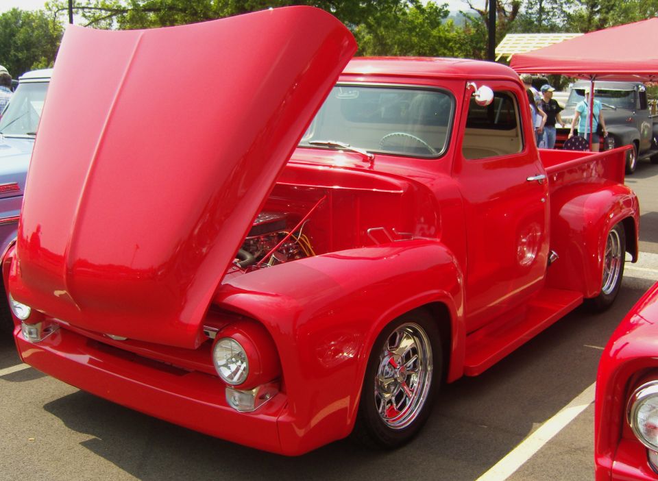 Red 1950s pickup truck with hood open, chrome wheels, and custom modifications