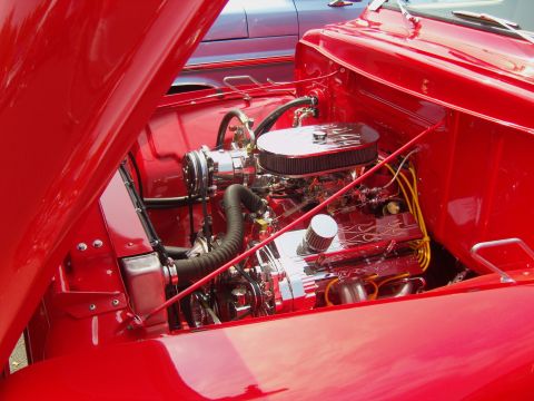 2007 Ford Mustang - The engine bay of a red classic car is shown with chrome accents and an open hood, with another vehicle visible behind it.
