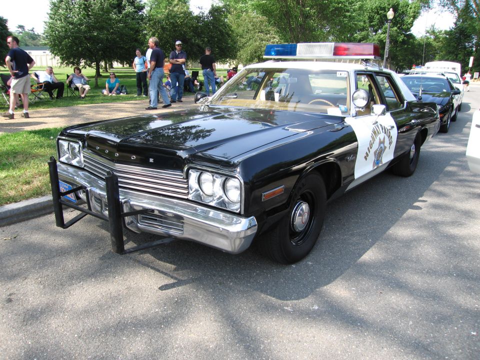 Black-and-white Dodge Highway Patrol sedan with push bar and spectators