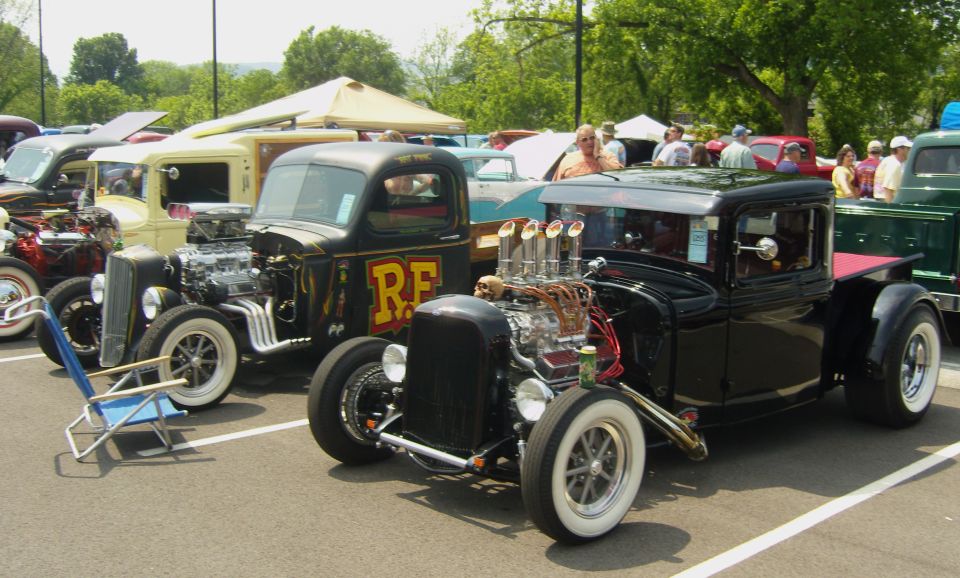 Two hot rod pickup trucks parked side-by-side, one black with a skull on the engine, the other black with yellow RF lettering