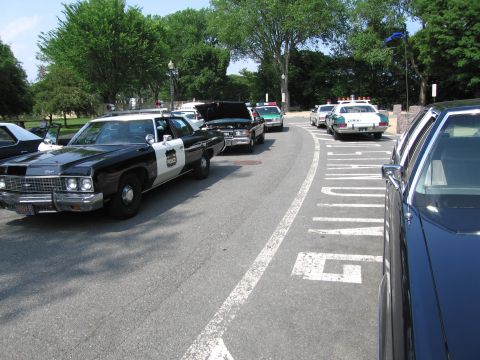 1991 Ford Crown Victoria - A line of police cars, including a black and white model in the foreground, are parked on a street.