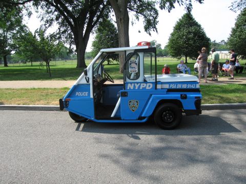 1991 Ford Crown Victoria - A three-wheeled NYPD vehicle is parked on a street with people in the background.