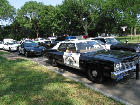 1991 Ford Crown Victoria - A collection of police vehicles, a mix of modern and vintage models, are parked along a roadside.