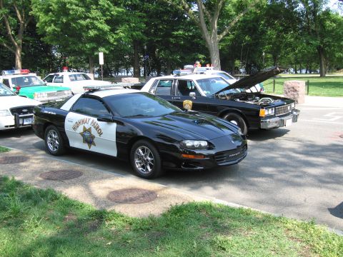 1991 Ford Crown Victoria - Multiple police vehicles, including a modern sports car and an older sedan, are parked outdoors.