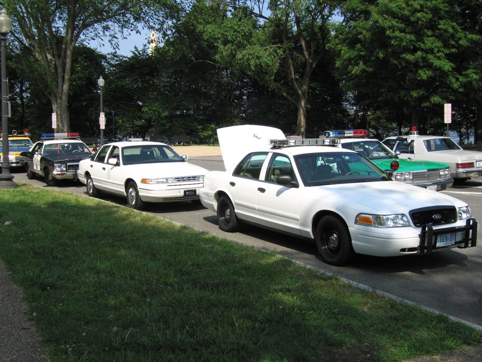 White Ford Crown Victoria patrol car with hood up beside other patrol cars