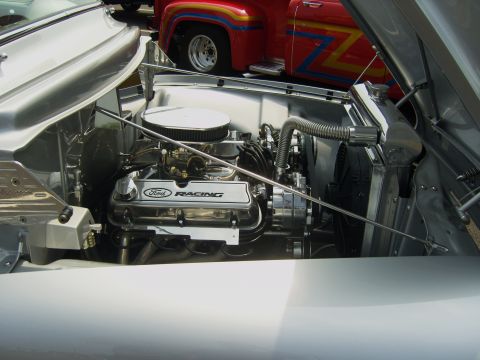 2007 Ford Mustang - The engine bay of a custom vehicle features a Ford Racing V8 engine, with another classic truck parked behind it.