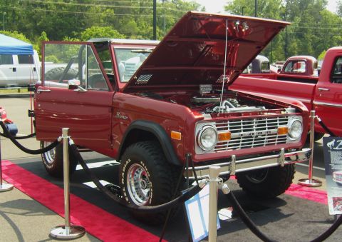 2007 Ford Mustang - Classic red Ford Bronco on display at an event, hood and door open, with a red pickup truck in the background.