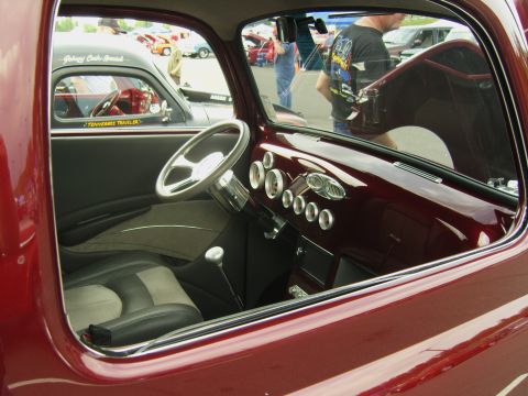 2007 Ford Mustang - Interior view of a custom maroon hot rod, a unique steering wheel and dashboard gauges. Another vehicle is seen in the background.