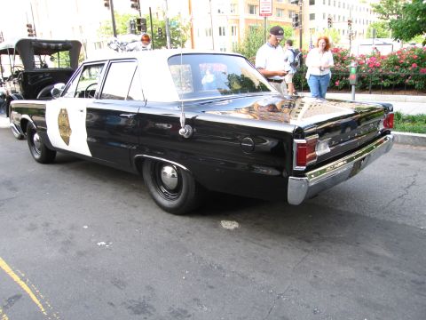 1991 Ford Crown Victoria - This police car, likely a 1967 Dodge, is seen from the rear quarter angle on a city street.