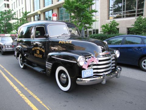 1991 Ford Crown Victoria - A vintage police car, marked 'Metropolitan 13 Police', is parked on a street next to a modern blue car.
