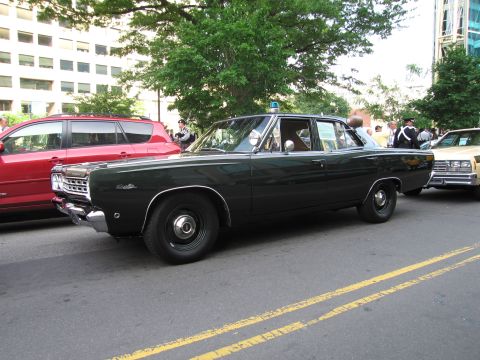 1991 Ford Crown Victoria - Side view of a vintage dark green police sedan with a light bar, parked on a street.