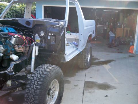 1985 Ford Bronco - This unfinished Ford Bronco body is in primer gray and features large off-road tires, with the engine exposed on the driver's side.