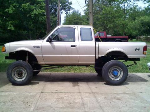 1997 Ford Ranger - A lifted gold 1997 Ford Ranger pickup truck is parked on a concrete surface with another truck in the background.