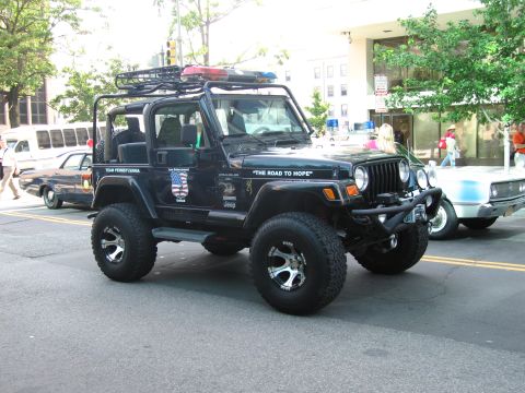 1991 Ford Crown Victoria - A black Jeep Wrangler is parked on a city street, equipped with a roof rack and emergency lights.