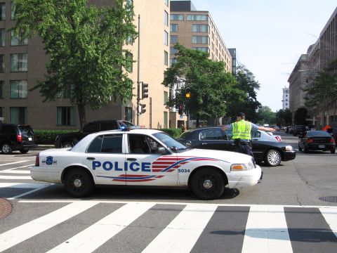 1991 Ford Crown Victoria - A police car is stopped at a crosswalk while a traffic officer directs traffic.