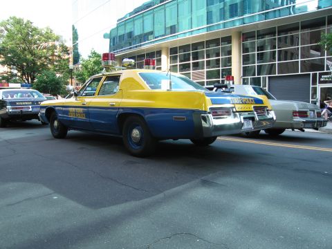 1991 Ford Crown Victoria - Two police cars are parked on a street in front of a modern building.
