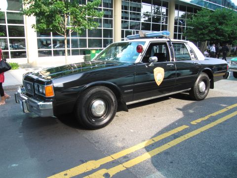1991 Ford Crown Victoria - This black police car, seen from a 3/4 front angle, has the distinctive body style of a 1980s vehicle, not a 1991 Ford Crown Victoria.