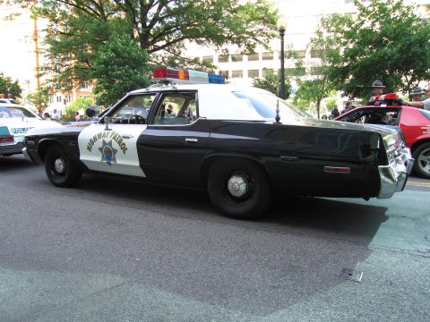 1991 Ford Crown Victoria - A black and white police car with a light bar on the roof is parked on a street.