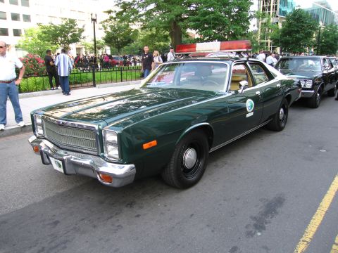 1991 Ford Crown Victoria - This 1977 Plymouth Gran Fury police car features a light bar and is parked in a line with other vehicles.