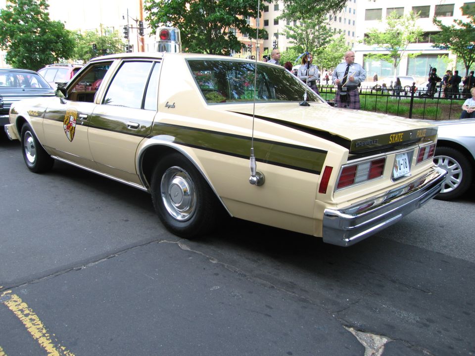 Tan and brown 'State Police' sedan rear three-quarter with light bar on city street