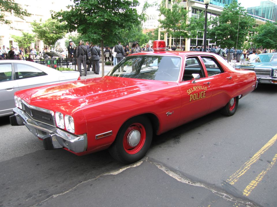 Red 'Selbyville Police' four-door sedan with single roof light parked on city street