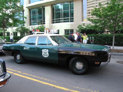 1991 Ford Crown Victoria - A two-tone police car with a light bar is parked on a city street.