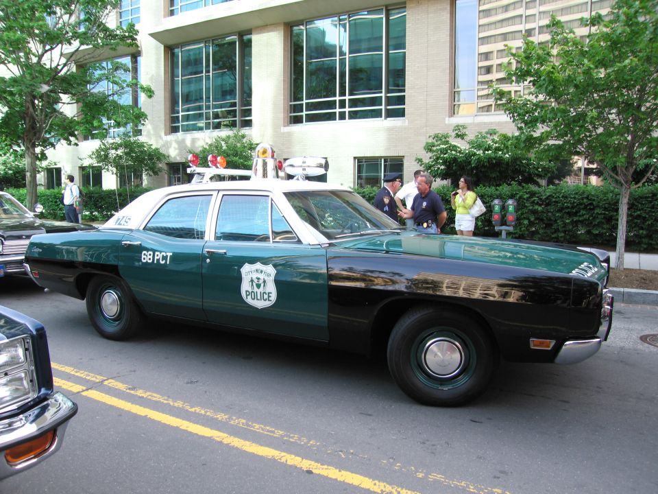 Green and white '68 PCT Police' sedan side view with roof lights on city street