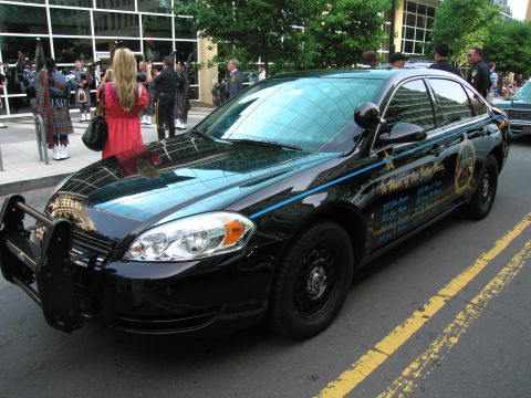 1991 Ford Crown Victoria - A police car is parked on a street with yellow lines, with people in kilts in the background.