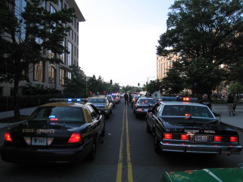 1991 Ford Crown Victoria - A line of police cars, including a 1991 Ford Crown Victoria, are stopped on a city street.