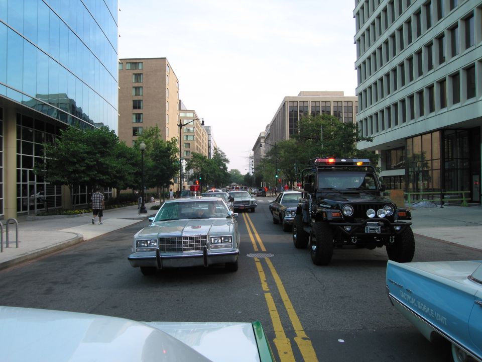Silver sedan and lifted black off-road truck driving down a city street
