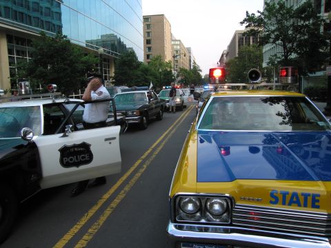 1991 Ford Crown Victoria - Police cars are stopped in traffic on a city street, with buildings lining the road.