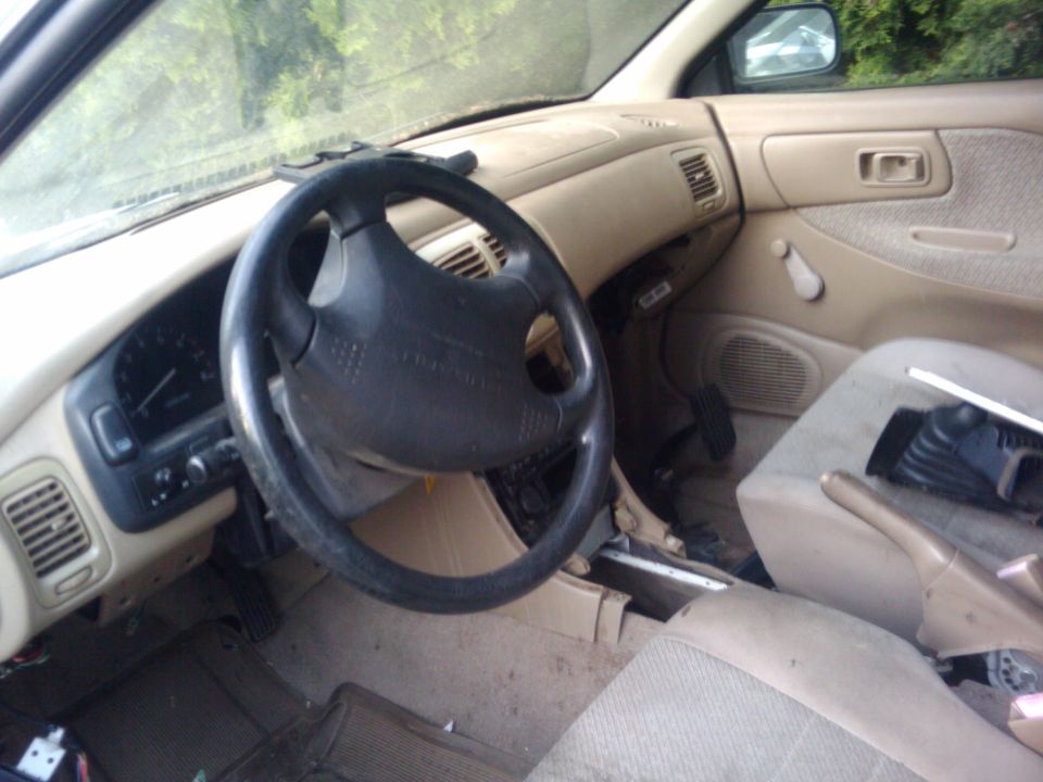 Interior shot of a car's dashboard, steering wheel, and passenger seat. The car appears older and somewhat worn