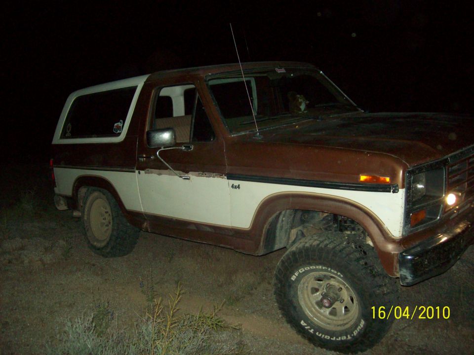 Brown and white 1985 Ford Bronco 4x4 parked off-road at night