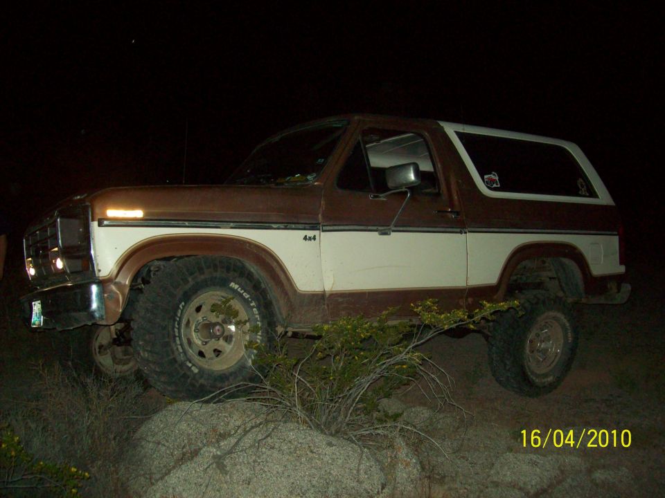 Brown and white 1980s Ford Bronco 4x4 parked on rocks at night. "4x4" badge visible