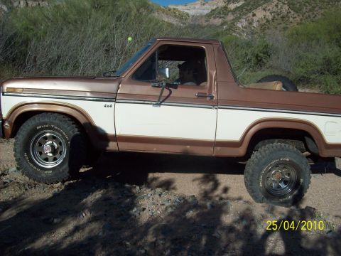 1985 Ford Bronco - This two-tone Ford Bronco is shown off-road with mountains in the background.
