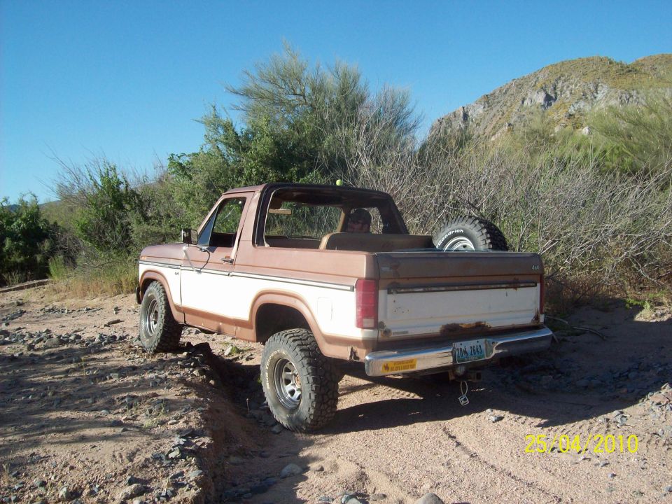 Brown and white 1980s Ford Bronco parked on a dirt road, rear view