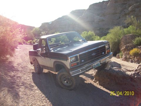 1985 Ford Bronco - This Ford truck is navigating a rocky, off-road trail under a bright sun.