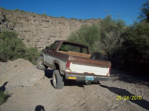 1985 Ford Bronco - This 1985 Ford Bronco navigates a rocky trail, showing its rear profile and spare tire mounted in the bed.
