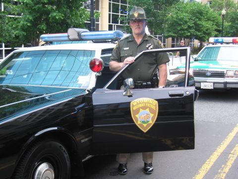 1991 Ford Crown Victoria - A Wyoming Highway Patrol officer stands beside a 1991 Ford Crown Victoria police car, with another patrol car visible in the background.