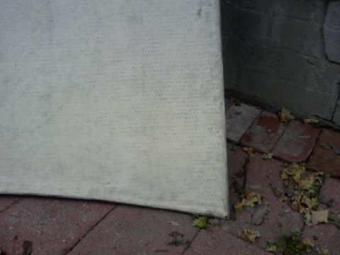 1990 Ford Bronco - A car cover is shown resting on a brick and concrete surface, obscuring the vehicle beneath.