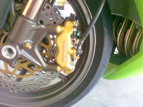 2005 Kawasaki Ninja R - A close-up view of a motorcycle's front braking system, highlighting the gold caliper and perforated disc.
