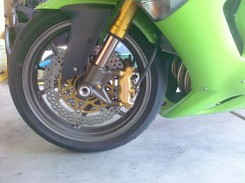 2005 Kawasaki Ninja R - Close-up of a motorcycle's front wheel assembly, showing the brake system and part of the green bodywork.
