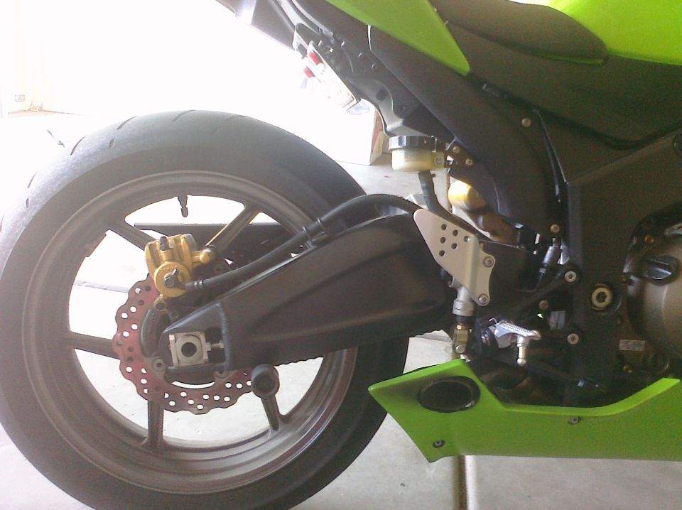 Motorcycle rear wheel with gold caliper and red disc brake, green fairing visible