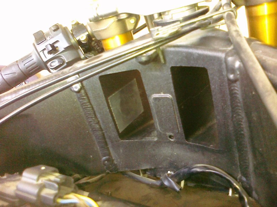 Close-up of a black motorcycle air intake box with visible welds and electrical connectors