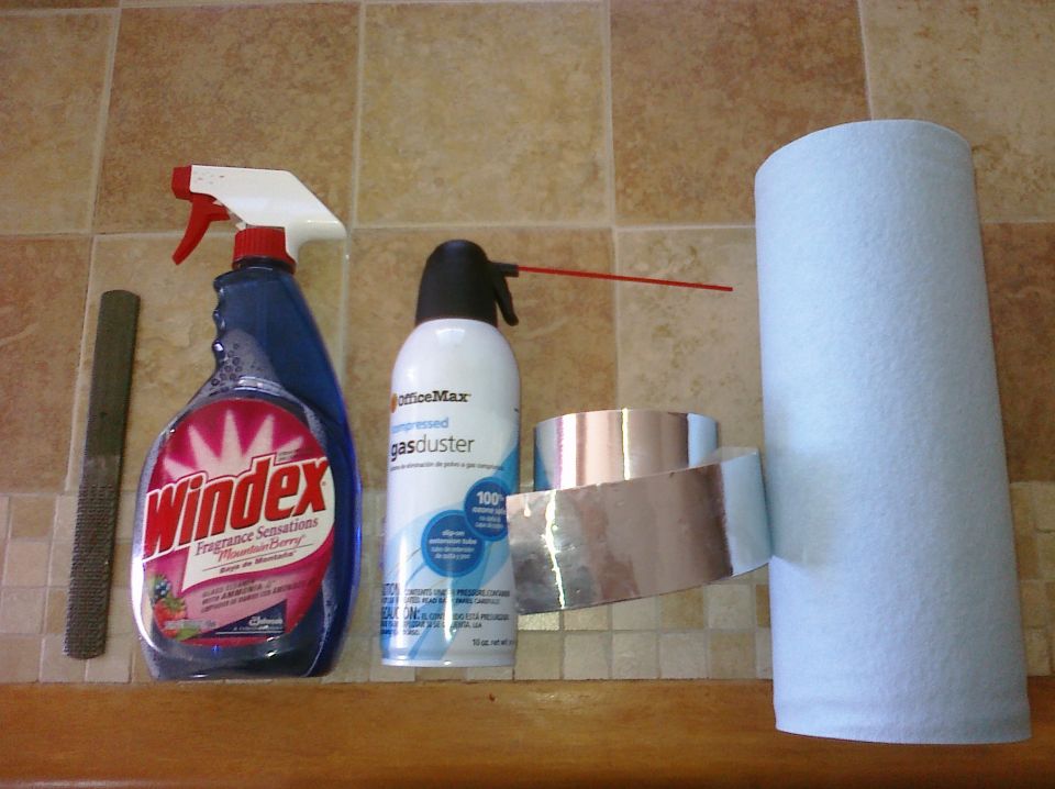Windex bottle, compressed air duster, foil tape, and paper towels on a tiled surface