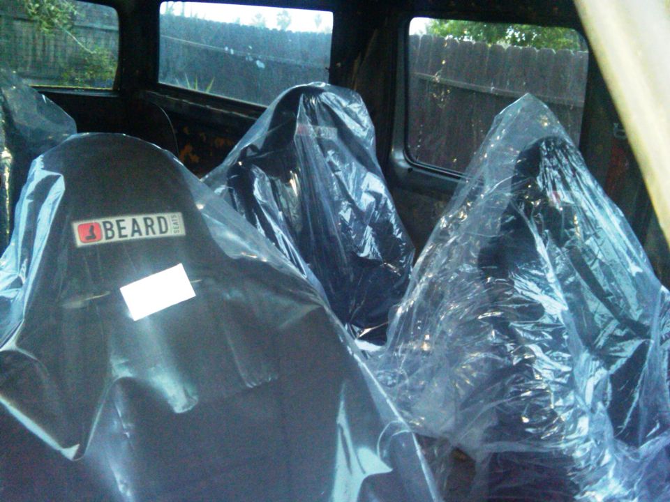 New black Beard bucket seats in factory plastic wrap sitting inside a stripped truck cab